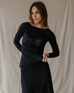 - Product: Lace Moonlight Black Top (visible as a fitted, long-sleeve lace top paired with a matching lace skirt in the photo)
- Intended audience: Women (model styling and feminine fit)
- Notable visible attributes: sheer black lace fabric with a delicate floral pattern, long sleeves, boat/soft scoop neckline, fitted silhouette, layering with a matching black lace skirt.