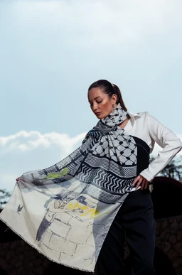 - Item: A lightweight scarf draped around a woman's shoulders, shown flowing slightly as she poses outdoors.
- Intended audience: Women, based on the model and styling.
- Visible attributes: Black, white, and light gray geometric and abstract print with hints of pale yellow; scarf appears airy and large, paired with a white blouse and dark pants for a chic, windy-day look. No brand names visible.