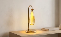 - What the product is: A decorative table lamp with a curved metal stem and a teardrop-shaped glass bulb.
- Apparent audience: Unisex (suitable for both men and women), based on neutral minimalist design and warm ambient glow.
- Notable attributes: Warm amber/golden glass bulb, brass/gold-toned metal stem and base, circular base plate, simple contemporary styling.