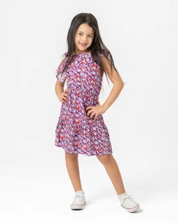 A lightweight girls’ sundress with a purple-pink floral print. The dress has a relaxed, above-the-knee silhouette with short flutter sleeves and a slightly gathered waist, styled with white sneakers as shown. Visible materials suggest a soft, breathable fabric (likely cotton or a cotton blend) in a bright, spring-time floral pattern with pink, purple, and white tones.