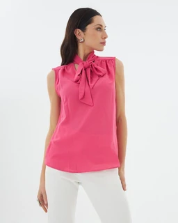 A sleeveless blouse in a bright pink color with a high neckline and a large fabric bow tied at the collar. The fit appears tailored through the torso with a clean, cropped-leaning silhouette, designed for a feminine, lightweight look. Notable details include the bow neck, smooth satin-like fabric, and a soft drape over the bodice, suitable for a women’s audience.