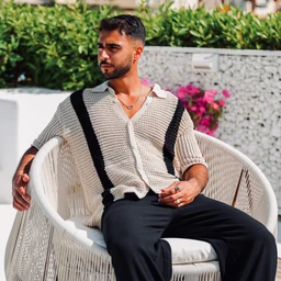 - A casually styled striped knitted shirt in a light beige base with bold black vertical stripes on the sides, worn open over a light top; short-sleeve, relaxed fit, and a loose, drapey knit. 
- Appears intended for men, based on the model’s styling and fit; the look is modern and loungey, suitable for casual or resort wear. 
- Notable details include the chunky knit texture, open collar with a V-neck, and contrasting black stripe accents that run along the front and sleeves, in a neutral beige/black color palette.
