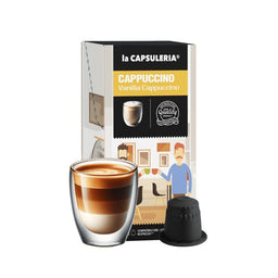 This is a capsule coffee product—Nespresso-compatible vanilla cappuccino capsules—shown with a single stacked-layer cup of layered cappuccino in a glass. The packaging features a black-and-yellow label and a cartoon-style illustration, suggesting a unisex audience. Notable visible attributes include the vanilla cappuccino flavor, compact capsule form, and a glossy coffee beverage with distinct crema on top.