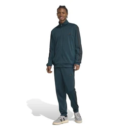 The image shows a full tracksuit consisting of a zip-up windbreaker-style jacket and matching jogger pants in a dark teal/blue color. It appears designed for men, judging by the model and styling, with a slim athletic fit, long sleeves, and a high collar; the fabric looks lightweight with a smooth, slightly shiny tricot texture. Notable details include a subtle three-stripe/branding motif on the chest and leg, and light-colored sneakers completing a casual athletic look.