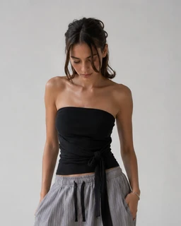 This is a black strapless tube top with a tie-front detail. It appears designed for a women’s audience, shown on a female model with a slim, strapless cut that emphasizes the shoulders and upper torso. Visible materials look like a smooth stretch fabric; the top has a form-fitting silhouette and a tie at the side, giving a gathered, wrap-like accent. The color is solid black, with a minimalist, chic style suitable for warm-weather or layering.