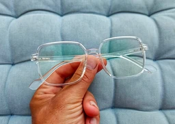 The product is a pair of clear, lightweight eyeglasses with oversized rectangular lenses. Intended for adults (likely unisex), based on neutral transparent frame styling and fit. Notable features include a transparent plastic frame, silver-tone hinges, and a subtle, modern square-lens shape suitable for screen use; the design emphasizes a lightweight, minimal look.
