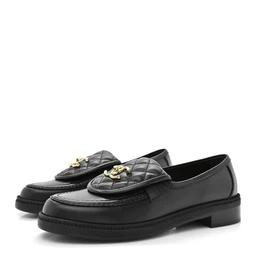 A pair of black quilted leather loafers with a classic penny-style silhouette. Appears designed for women, given the refined quilted upper and gold-toned turnlock hardware on the vamp, with a low stacked heel and cushioned sole. Notable materials include smooth black leather with quilted stitching and gold-tone hardware on the front, in a traditional loafer style.