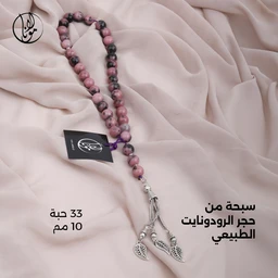 - المنتج ظُهرت منه سُبحة (مسبحة) من حجر الرودونايت الطبيعي، مكونة من 33 حبة بحجم تقريبي 10 مم. اللون الغالب وردي مع تدرجات داكنة وفاتحة، وتوجد حبات بنية داكنة/رمادية في بعض السلاسل.
- التصميم مخصص للنساء/البنات (مظهر أنثوي، مع سلاسل خيط متدلٍّ وتطريز فضّي في المعلقات)، مع قلادة خيط وتبنّيات فضية زخرفية تشبه الفلّات والورود.
- المواد والمظهر: حجر الروديونايت الطبيعي كحجر أساسي، حبات مستديرة لامعة، خيط مركزي باللون الأرجواني/النيلي، مع تعليقة فضية من ثلاث أشكال مكسوة بتعليقات نباتية (أوراق). اللون العام وردي-وردي داكن مع لمسات فضية.