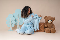 - What it is: A baby boy fleece pajama set being worn and displayed by a child model in matching blue loungewear. The set includes a long-sleeve top and pants, made from soft, cozy fleece.
- Audience and style: Intended for babies/young children (unisex-leaning toward boys based on typical product naming); pastel blue color, comfortable lounging style, with a playful, cozy winter vibe. 
- Notable attributes visible: Soft light blue fleece fabric, long-sleeve top and pants, model holding a matching fleece jacket, backdrop includes cutout trees and a large teddy bear prop, overall cute, indoor sleepwear presentation.