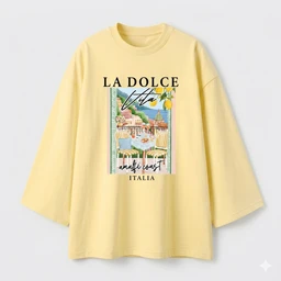A light yellow oversized T-shirt featuring a graphic print on the front. The design shows a colorful illustration with a coastal scene, framed by text elements, suggesting a casual, beachy aesthetic. Visible attributes include a relaxed fit, long sleeves, soft cotton-like fabric, and a pale yellow colorway. Suitable for a unisex or women’s casual wear look.