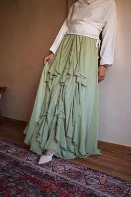 - What is shown: A women's skirt with a high waist and multiple cascading ruffle layers, finished to floor-length with a soft, flowing drape.
- Intended audience and styling cues: Women's or unisex-leaning attire, styled for a formal or dressy casual look with a white long-sleeve blouse tucked into the skirt.
- Visible attributes: Lime green (minty) color, layered ruffles along the hem that create volume, lightweight, airy fabric with a flowy silhouette. The model is wearing white pointed-toe shoes.