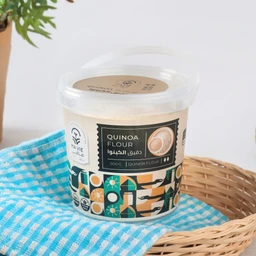 - Product: A tub of quinoa flour.
- Audience and styling: Appears unisex; presented as a kitchen staple with a clean, modern label on a neutral backdrop, placed on a blue patterned cloth and woven basket for a home-use context.
- Visible attributes: Plastic screw-top tub with a beige label reading “Quinoa Flour” and a small image of a bowl; decorative geometric pattern on the lower half of the container; bag size 500 g (as labeled). Material colour is off-white flour inside the tub.