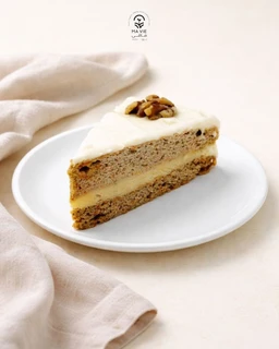 - What it is: A slice of gluten-free carrot cake with cream cheese frosting and a decorative nut topping, served on a white plate.
- Audience and styling cues: Appears intended for adults (both genders) given the neutral, elegant presentation; simple, minimalist styling with light beige backdrop and soft fabric accents.
- Notable attributes: Carrot cake layers with a pale yellow cream filling/frosting, visible walnuts on top, and a smooth white frosting layer. The cake has a dense, moist texture typical of gluten-free recipes. No branding visible.