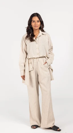 - What the product is: A beige linen set consisting of a long-sleeve button-up shirt and wide-leg pants, both with a subtle vertical stripe pattern. It appears to be a relaxed, coordinated lounge-to-casual outfit with a matching belt at the waist.
- Intended audience: Women (based on the model and styling).
- Notable attributes: Linen fabric in a light beige color, vertical stripe pattern, relaxed fit, button-front shirt, wide-leg pants with a tied belt, and a light, casual, breathable look.