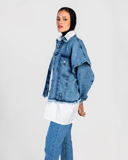 A denim outfit featuring an oversized blue denim jacket layered over a white shirt or blouse and matching straight-leg blue jeans. The ensemble appears styled for women, with a loose, relaxed fit and a light-wash denim tone. Notable materials include classic denim with visible stitching; the look emphasizes a double denim/denim-on-denim style with a casual, contemporary vibe.