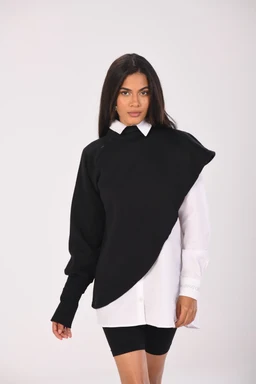 - Product: A two-tone poncho or oversized top layered over a white shirtdress look, featuring a black cape-like overlay with an asymmetrical hem over one shoulder, paired with a long-sleeve white shirt underneath.
- Audience: Women, judging from the model and styling.
- Notable attributes: Black upper overlay with a curved, diagonal edge, white long-sleeve shirt underneath visible at the collar and sleeves, a crisp white shirt collar peeking out, and a sheer, shorter bottom appearance suggesting a layered poncho over a shirt dress; the overall look is monochrome black and white with a modern, architectural silhouette.