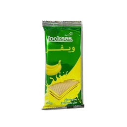 This is a packaged banana wafer snack. The visible packaging features a green and yellow design with a banana graphic and a wafer biscuit image, suggesting a banana-flavored, light, crisp wafer. The scene appears to be a single, upright snack bar aimed at a general audience, with no brand identification beyond the word “Jockses” on the wrapper.