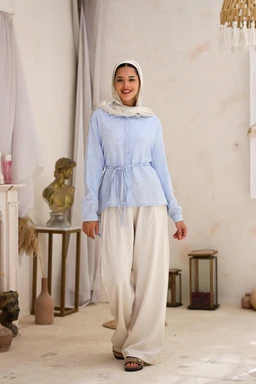 - Product: A light blue, long-sleeved hoodie or tunic-style top with a drawstring waist, paired with wide-legged cream or off-white pants. The model wears a white headscarf, suggesting modest or hijab-friendly styling.
- Intended audience: Women's or unisex modest fashion, with a relaxed, comfortable fit suitable for casual/ lounge wear.
- Notable attributes: Soft, textured fabric in a pastel blue; waist ties for silhouette shaping; wide-leg, flowing cream pants; simple, clean styling with neutral accessories and a light, airy backdrop. No branding visible.