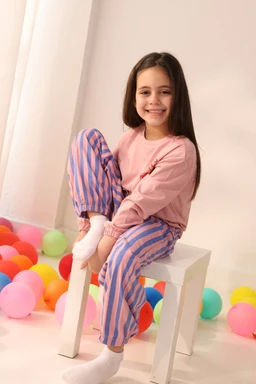 - The product appears to be a long-sleeve top paired with striped pajama pants, designed for kids. The model is a young girl, indicating a girls’ or unisex kids’ size range.
- Notable visible attributes: soft pink top, blue-and-pink vertical striped pants, white socks. The outfit has a playful, cozy loungewear style with pastel colors suitable for children.