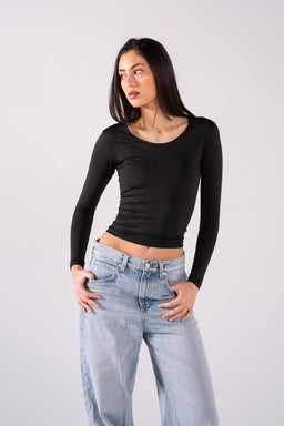 - Description: A woman wearing a fitted black long-sleeve top with a wide, rounded neckline and ruched sides. The top is paired with light-wash, relaxed-fit jeans.
- Audience and style cues: Designed for women, with a sleek, minimalist chic vibe suitable for casual or streetwear looks.
- Notable materials and attributes: Black stretchy knit fabric; long sleeves; wide scoop/boat neckline; cropped length with ruching at the sides; light blue denim jeans with a high-rise feel.