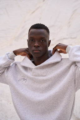 - Description: A light heather gray pullover with a wide, folded collar and a half-zip neckline, worn by a male model. The fabric looks soft and fleece-like, suggesting a cozy, casual sweatshirt/jumper style.
- Audience and styling: Appears designed for men; the relaxed fit and neutral tone suit casual, lounge, or streetwear looks. The model’s pose highlights the oversized collar and roomy silhouette.
- Notable attributes: Soft gray color, fleece-like texture, oversized/loose fit, folded collar with a subtle front logo or script embroidery on the chest. No branding visible beyond the small script, no additional patterns or graphics.