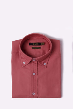A neatly folded brick-red oxford shirt with a button-down collar and white buttons. Likely intended for men (based on cut and classic button-down styling). Visible details include a solid cotton-oxford fabric in a warm brick hue, standard placket, and collar with buttoned points, presenting a crisp, casual-to-smart look.