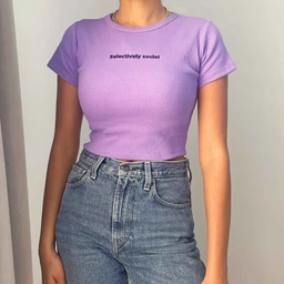 A cropped, ribbed knit T-shirt in a pastel lavender color with a close, fitted silhouette. Appears intended for women or girls, due to the short length and body-skimming cut, styled with high-waisted jeans in the photo. Notable details include a crew neck, short sleeves, and a small text logo reading “selectively social” centered on the chest. Material looks like stretch cotton or ribbed jersey with a smooth, matte finish.
