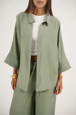 This is a women's. A loose, oversized button-front shirt layered over a white top, paired with matching wide-leg pants. Notable attributes: soft, pale sage linen-like fabric with a subtle sparkle or dot texture; relaxed shawl collar and wide, three-quarter sleeves that can be rolled, giving a casual yet polished look. The outfit emphasizes a cohesive, breathable linen-style set in a light green shade.