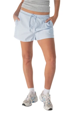 Product: Scandi blue shorts

- Appears to be a pair of light blue, casual drawstring shorts worn by a female model. The shorts have a relaxed fit with a mid-thigh length, side pockets, and an elastic/wixed drawstring waistband. The model is wearing a cropped top, white crew socks, and athletic sneakers, suggesting a sporty casual vibe.
- Notable attributes visible: light blue color, lightweight woven fabric, drawstring at the waist, relaxed/short length, side pockets, matching white socks and sneakers for styling. The overall look is casual, summery, and suitable for active or lounge wear.