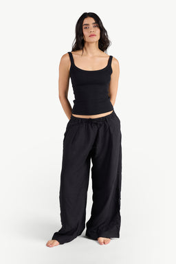 - What it is: A pair of black linen pants worn by a female model. The pants are loose-fitting with a relaxed, wide-leg silhouette and an elastic waistband.
- Intended audience and styling cues: Women's or unisex, based on the model styling; casual, comfortable loungewear or summer wear.
- Notable attributes visible: Material appears lightweight and breathable linen, solid black color, drawstring-less elastic waistband, ankle-grazing to full-length wide legs, no visible pockets or embellishments. The model wears a black sleeveless cropped top to emphasize the relaxed fit.