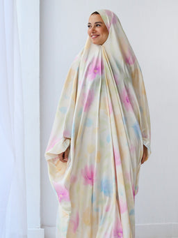 This appears to be a pastel-patterned khimar (slip-on Islamic head covering) worn by a female model. The styling is loose and draped, covering the entire body with a soft, multi-color tie-dye look. Visible material looks lightweight and flowing, with pastel pink, blue, yellow, and cream tones. Audience: women. Notable attributes: pastel tie-dye pattern, full-body drape, slip-on khimar design, light and breathable fabric. Color palette is soft, muted pastels.