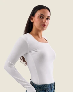 A fitted long-sleeve top with a squared, wide neckline. The model suggests a women's audience; the top is solid off-white, appears to be a stretchy knit or cotton-blend fabric with a smooth, clean finish and a slim, body-skimming silhouette.