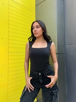 A fitted black top with a square neckline and wide shoulder straps, shown on a female model. The style appears to be a sleeveless, body-con tank suitable for casual or night-out wear, paired with dark high-waisted cargo-style pants. Visible details include a smooth, stretch fabric with a clean solid black colour and minimal seam lines.