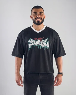 A black graffiti-style jersey T-shirt with a bold graphic across the chest featuring light blue and white lettering and drippy accents. The fit appears relaxed with short sleeves and a white V-neck trim, modeled by a man, suggesting a men’s target audience. Notable elements include the oversized short-sleeve silhouette, graphic print, and contrast white neckline, all in cotton-like jersey fabric.