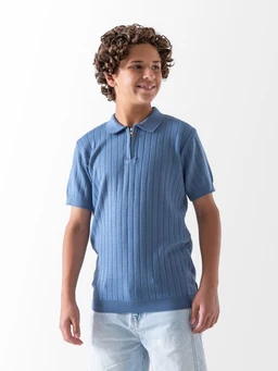 This is a knit polo shirt. It appears designed for boys, judging by the model’s age and fit, with a short-sleeve silhouette and a classic polo collar featuring a light placket. The fabric is a textured, vertical rib knit in a medium blue shade, with a slightly longer hem and a neat, casual look.