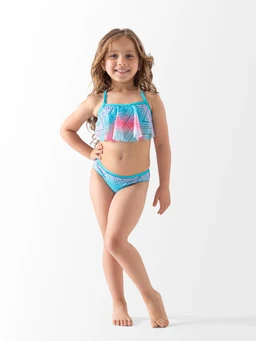 This is a two-piece youth swimsuit with a ruffled, off-shoulder style top and matching bikini bottoms. The apparent audience is girls, based on the young model and playful pastel colors. Notable features include a blue-toned geometric pattern, bright pink accents on the top, and a halter-like strap design with a cropped top and bikini bottom. Material appears to be stretchy swim fabric suitable for kids.