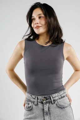 A sleeveless fitted tank top in a dark gray color, shown on a female model. It has a smooth, double-layer knit appearance with a high, crew neckline and cropped-length silhouette that pairs with light-wash denim jeans. The styling emphasizes a clean, minimalist, everyday casual look with a solid monochrome fabric.
