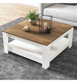 The image shows a modern coffee table with a two-tone design: a warm wood-toned rectangular tabletop and a bright white lower frame and legs. It appears to be intended for a living room setting, suitable for a unisex audience judging by its neutral style and clean lines. Notable features include a wood veneer top, white painted base with an open lower shelf, and simple decorative items arranged on top (plant, candle holder, and lantern).