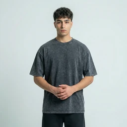 This is a washed, oversized unisex T-shirt in dark grey. It features a relaxed fit with dropped shoulders and a slightly faded, vintage wash, styling suitable for casual everyday wear. Visible attributes include mid-grey/blackwashed cotton fabric, crew neck, short sleeves, and knee-to-waist length on the model, with no visible logos or branding.