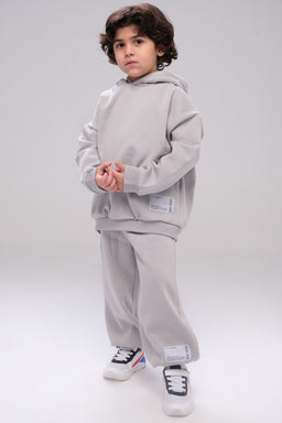 - What it is: An unisex oversized sweatshirt and sweatpants set in light silver/gray. The model wears a matching hoodie and baggy jogger-style pants with visible cuffs. 
- Audience and styling cues: Designed for unisex wear; the relaxed, oversized cut and neutral gray color suggest a casual, streetwear or lounge set. 
- Materials and details: The fabric appears soft and thick (fleece-like); the set features a hoodie with a front pocket and ribbed cuffs, plus elastic waistband joggers with cuffs. The look is completed with white sneakers for a clean, minimal aesthetic.