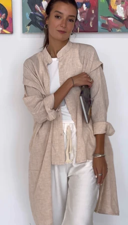 - What the product is: A long, lightweight linen-like button-front shirt or lightweight duster layered over casual wear.
- Apparent audience: Women (based on fit, styling, and pairing with a white top and light trousers).
- Notable attributes: Soft beige/stone color, relaxed, oversized fit with rolled sleeves, long hem, and a drapey, casual vibe. Visible materials suggest a breathable, linen-like fabric; styled with a white top and light drawstring-waist pants for a breezy, minimalist look.