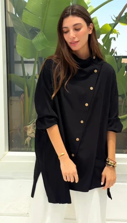 Product is a loose, black asymmetrical top with a stand-up collar and button-front detail. Intended for women, featuring rolled-up long sleeves and a relaxed, oversized silhouette with side slits. Visible attributes include a high-neck, button placket with multiple gold-toned buttons, lightweight fabric, and a draped, tunic-like cut paired with white bottoms in the photo. Material appears lightweight, flowy, likely cotton or a similar weave, in solid black.