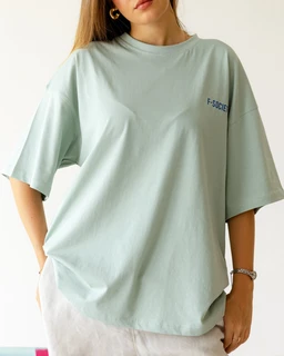 - What it is: A loose-fit oversized short-sleeve T-shirt in a light sage green color.
- Audience and styling cues: Designed for a unisex or relaxed casual look, modeled on a person with a relaxed pose; short sleeves with a dropped shoulder and a roomy, boxy cut.
- Notable attributes: Light pastel green/blue tone, soft cotton jersey appearance, crew neck, small text graphic on the left chest reading “FASCJOL” (partial visibility). The hemline is slightly uneven due to the oversized fit.
