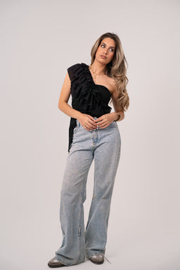- A black one-shoulder top with a large ruffled asymmetrical neckline and wrap/tie detail at the waist. 
- Intended audience: women's fashion. 
- Visible attributes: solid black fabric, one-shoulder style, prominent ruffles, wrap/tie at the side, cropped fit, paired with light-wash wide-leg jeans in the photo for styling. No brand visible.