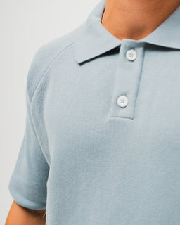 - What the product is: A polo-style knit top in light blue-grey, featuring a classic polo collar and a short placket with two buttons.
- Audience and styling: Appears designed for adults (unisex leaning toward a modern, casual look) with a relaxed fit and short sleeves suitable for everyday wear.
- Notable attributes: Knit texture with a smooth, lightweight yarn, ribbed sleeve edges, and a clean, minimalist polo collar in a matching blue-grey shade. No visible branding.