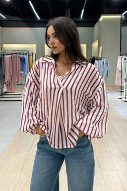 - Product: Relaxed striped collared blouse.
- Audience: Women (based on the model and styling).
- Notable attributes: Loose, oversized fit with voluminous long sleeves; white base with red vertical stripes; collared neckline with a short V/unfinished placket; lightweight woven fabric. Color palette is red and white, with a casual, breezy striped blouse appearance.