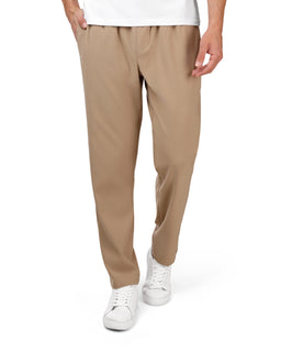 - What it is: A pair of beige/taupe soft sweatpants worn by a male model, styled with a white t-shirt and white sneakers.
- Audience/style cues: Men’s/unisex casual loungewear fit, relaxed straight-leg cut.
- Visible details: Elastic waist with drawstring (not visible but implied by sweatpants style), smooth soft fabric, side pockets, beige/tan color, white sneakers completing a casual look. No branding visible.
