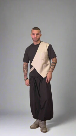 - What the product is: A men's fashion outfit featuring a color-blocked sleeveless top layered over a simple dark T-shirt, paired with voluminous drop-crotch pants and light sneakers.
- Apparent audience: Men's.
- Notable visible attributes: Beige geometric panel vest over a dark short-sleeve shirt, diagonally angled panel design, oversized loose-fitting black/brown pants with a gathered or dropped crotch, light beige sneakers, and minimal accessories (bracelets). The look has a contemporary, streetwear-inspired style with a muted, earthy color palette.
