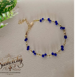 A delicate bracelet featuring small cobalt blue beads spaced along a fine gold-tone chain. The design appears unisex and lightweight, with blue round beads linked by tiny gold spacers and a short extender chain with a clasp. Notable attributes include the deep blue color of the beads, gold-tone metal findings, and a simple, elegant style suitable for everyday wear.