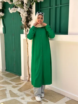 - Product: A plain long shirt-dress in a vivid green color. It has a button-down front with a simple, modest silhouette.
- Target audience: Women (modest, full-length style with a hijab suggests a women's or modestwear audience).
- Notable attributes: Long, loose fit with full-length sleeves; light gray wide-leg pants and white sneakers shown for styling; crisp, solid green fabric; white sunglasses perched on head; beige hijab. No visible branding.